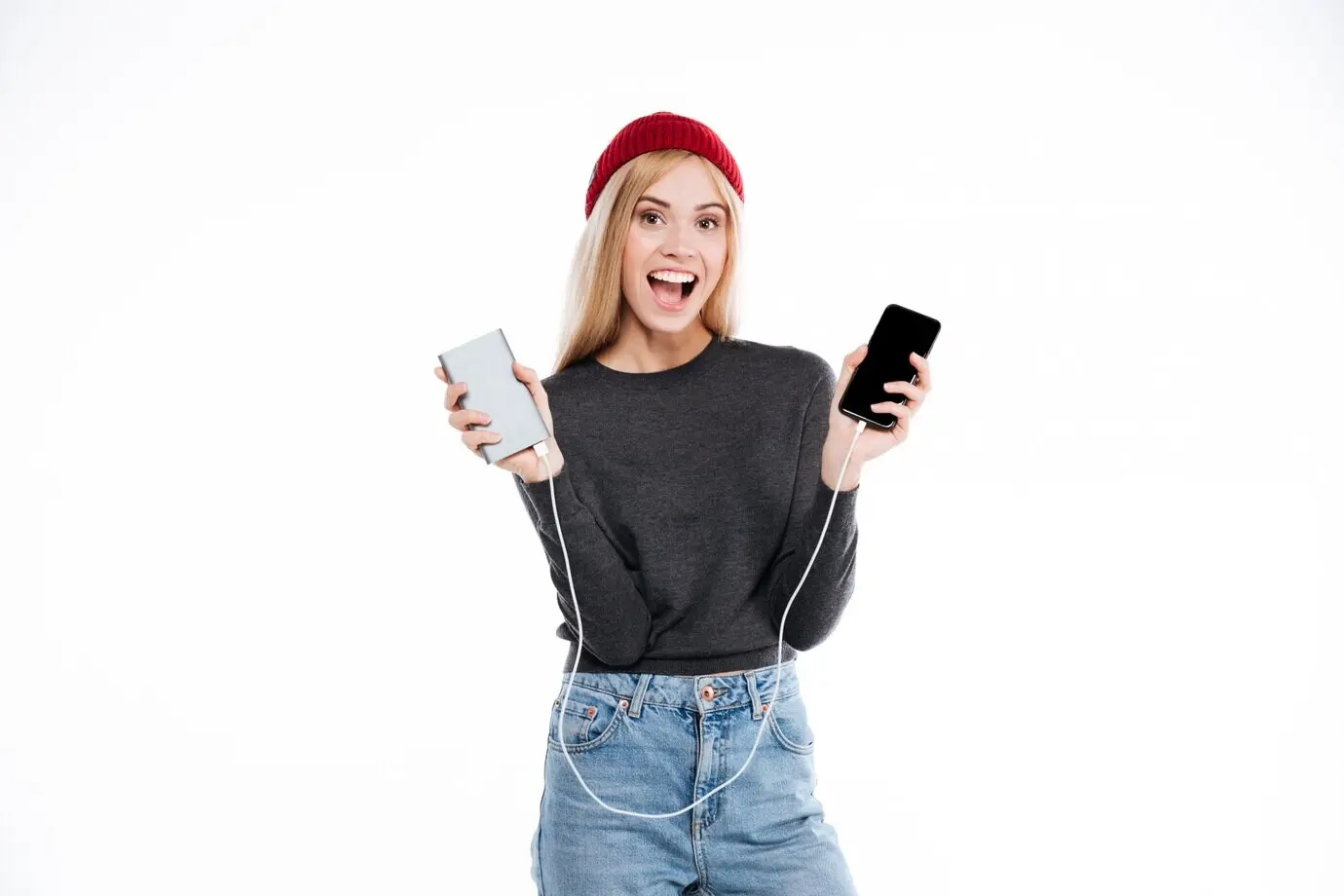 A woman in a sweater holds a power bank and a smartphone.