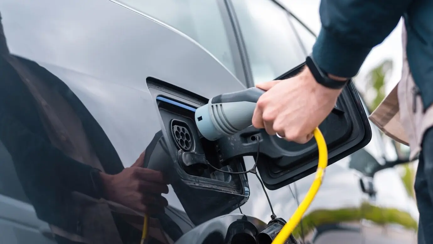 A man connecting a charger to an electric car at a charging station.