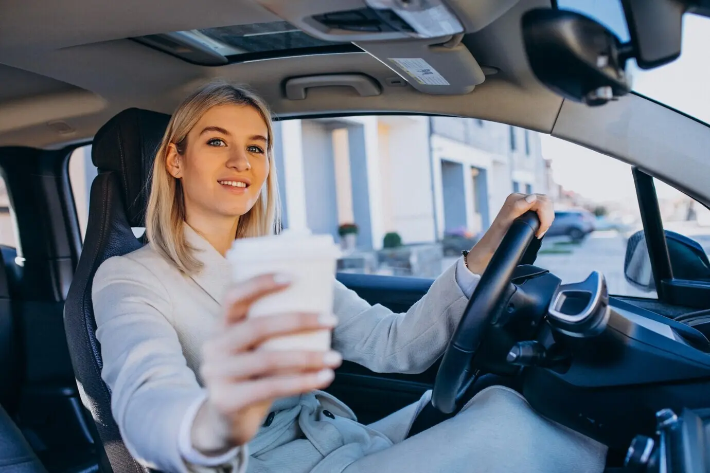 Woman sitting inside an electric car while it charges, with a coffee cup